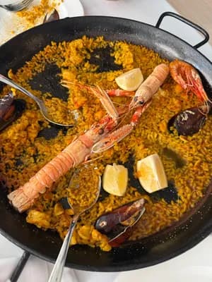 A pan of paella with seafood and lemon slices.