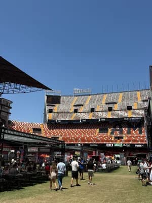 A sunny day at a large stadium with colorful seating and a crowd gathered in the foreground.