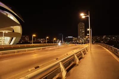 A bridge at night with streetlights and a modern building in the background.