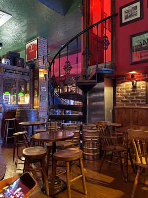 Intérieur d'un pub rustique avec des meubles en bois et un escalier en colimaçon.