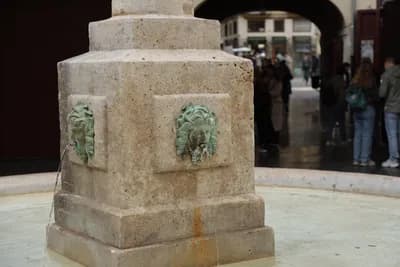 Close-up of a stone fountain with bronze lion heads.