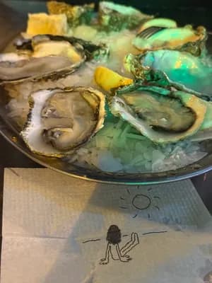 Plate of oysters on ice with lemon wedges and a napkin with a drawing of a sun and a person.