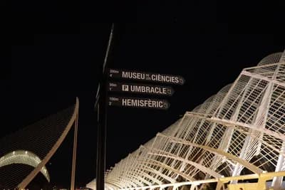 Directional signpost at night with illuminated text pointing to Museu de les Ciències, Umbracle, and Hemisfèric.