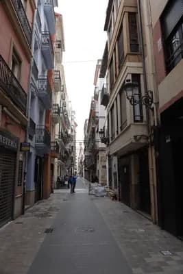 Narrow street with colorful buildings in Valencia, Spain, featuring a person walking in the distance.