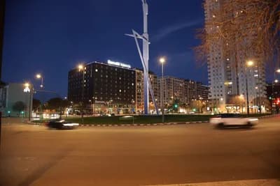 A nighttime urban scene with illuminated buildings and a sculpture in a roundabout.