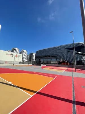 A vibrant basketball court with a modern architectural structure in the background and a clear blue sky above.
