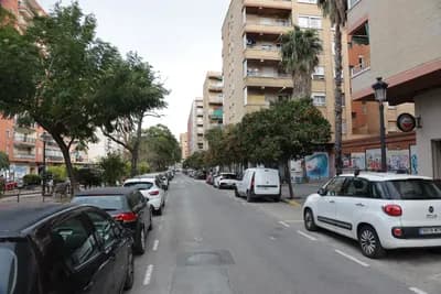 Parked cars and residential buildings on a street.