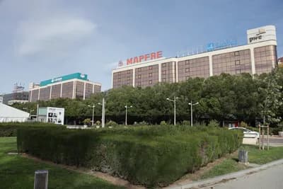 Large building with MAPFRE signage, surrounded by trees and urban architecture.