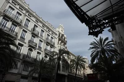 Palm trees and ornate balconies under a cloudy sky.