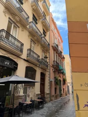 Narrow street with pastel buildings, balconies, and outdoor seating.