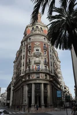 Historic building with ornate architecture and flying flags, framed by palm trees and a clear sky.
