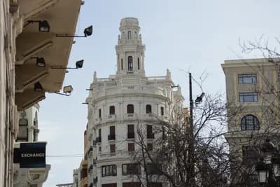 A white, ornate building with a curved facade and a clock tower against a clear sky.