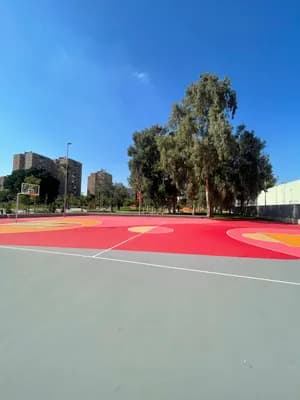 A vibrant basketball court with red and yellow markings under a sunny sky.