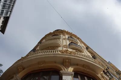 Close-up of an ornate building facade with balconies and decorative elements under a cloudy sky.