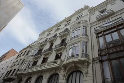 A white building with decorative balconies and windows against a partly cloudy sky.