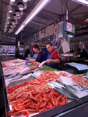 Deux vendeurs arrangent des fruits de mer à un stand de marché sous des lumières vives.