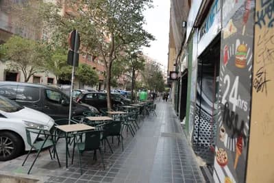 Outdoor seating area with tables and chairs along a sidewalk in an urban setting.