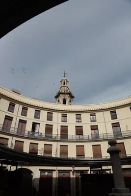 A curved building with a clock tower under a cloudy sky.