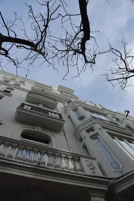 A white building with balconies and a bare tree against a blue sky.